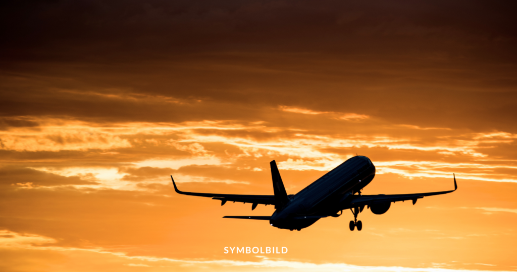 Das Bild zeigt ein Flugzeug im Silhouettenstil vor einem lebhaften orangefarbenen Himmel. Das Flugzeug befindet sich im Startvorgang, da das Fahrwerk sichtbar und ausgefahren ist. Der Farbverlauf des Himmels von dunkel bis hellorange bietet eine dramatische Kulisse für die Silhouette des Flugzeugs. Abschiebung Symbolbild