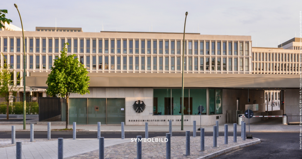 Das Bild zeigt ein modernes Gebäude mit einem klaren Himmel darüber. Die Architektur zeichnet sich durch eine lange, horizontale Struktur mit gleichmäßig verteilten Fenstern aus. Ein überhängendes Obergeschoss schafft einen überdachten Bereich im Erdgeschoss. Es handelt sich um den Neubau des Bundesinnenministeriums am Kanzlergarten. Compact Verbot Symbolbild