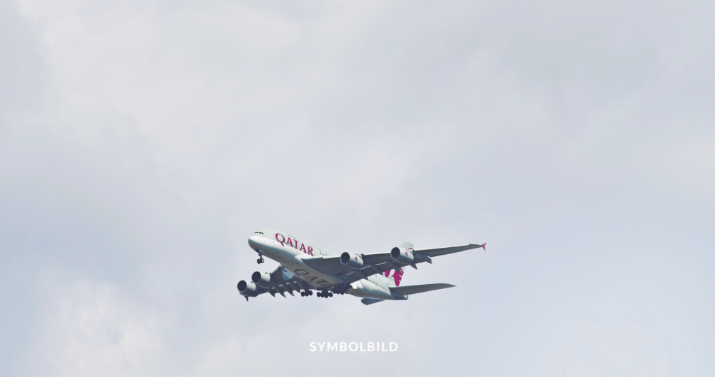 Das Bild zeigt ein Flugzeug von Qatar Airways im Flug vor einem bewölkten Himmel. Am unteren Rand des Bildes steht das Wort “SYMBOLBILD”. Abschiebung Symbolbild