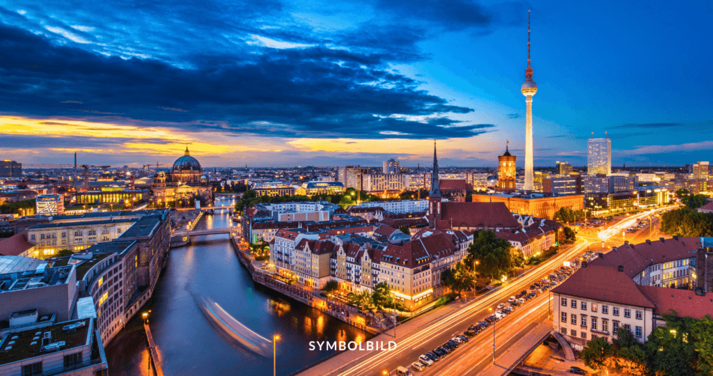 Das Bild zeigt eine Panoramaansicht von Berlin. Die Skyline der Stadt ist zu sehen, mit markanten Gebäuden. Der Fernsehturm ist deutlich sichtbar und ragt im Hintergrund empor. Die Spree fließt durch die Stadt, mit Brücken, die darüber führen, die sich auf der Wasseroberfläche spiegeln. Entlang der Ufer stehen Gebäude verschiedener architektonischer Stile. SYMBOLBILD Berlin Springer