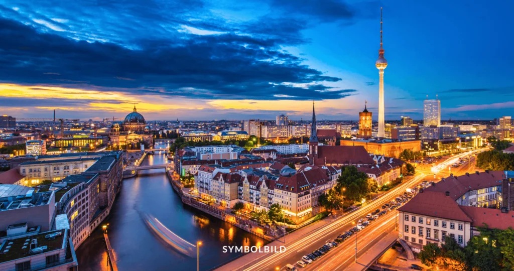 Das Bild zeigt eine Panoramaansicht von Berlin. Die Skyline der Stadt ist zu sehen, mit markanten Gebäuden. Der Fernsehturm ist deutlich sichtbar und ragt im Hintergrund empor. Die Spree fließt durch die Stadt, mit Brücken, die darüber führen, die sich auf der Wasseroberfläche spiegeln. Entlang der Ufer stehen Gebäude verschiedener architektonischer Stile. SYMBOLBILD Berlin Springer