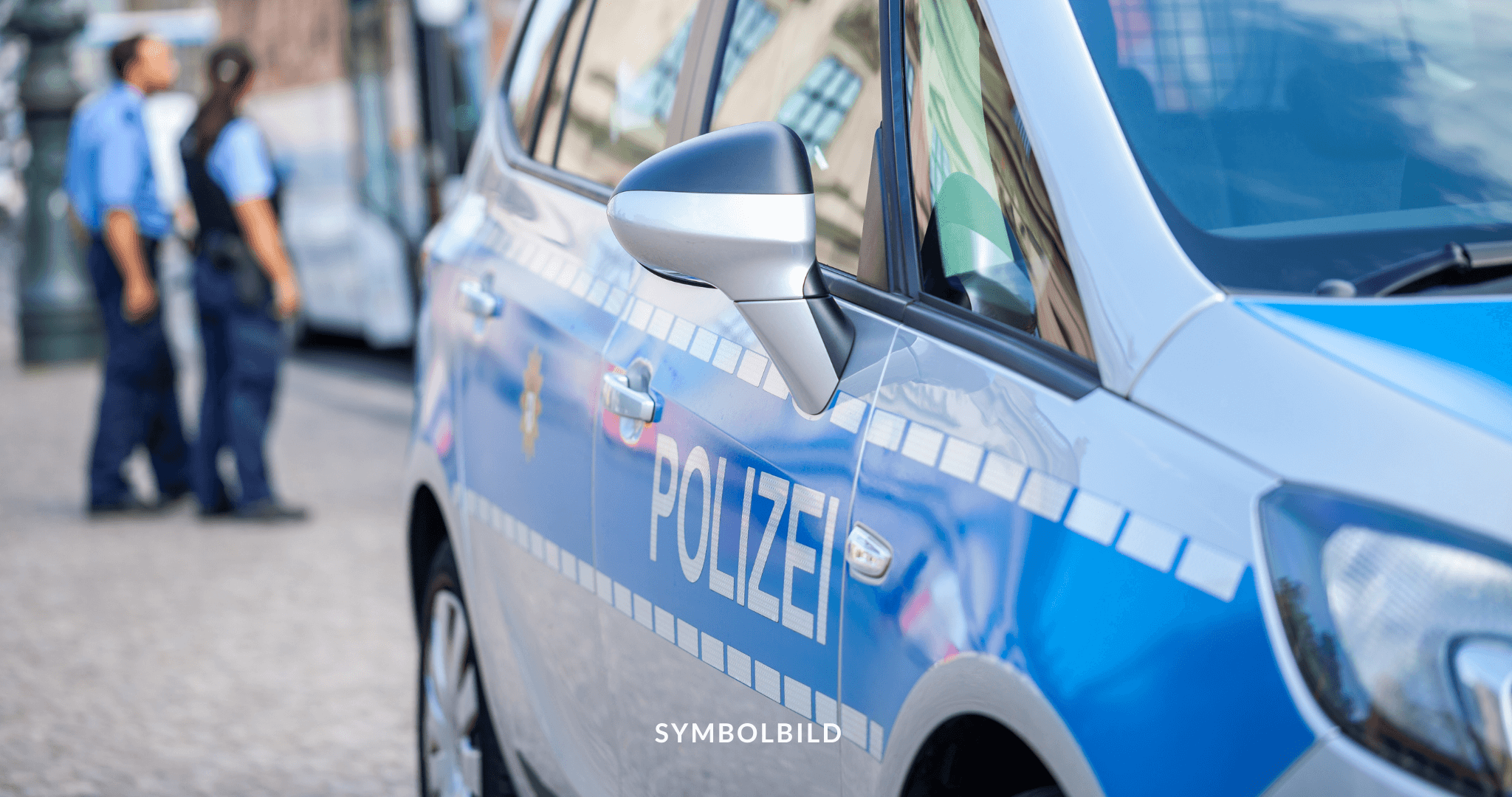 Das Bild zeigt einen Teil eines Polizeiautos mit dem Schriftzug “POLIZEI”. Im Hintergrund sind zwei Personen in einer Polizei-Uniform zu sehen. Polizei Solingen Symbolbild