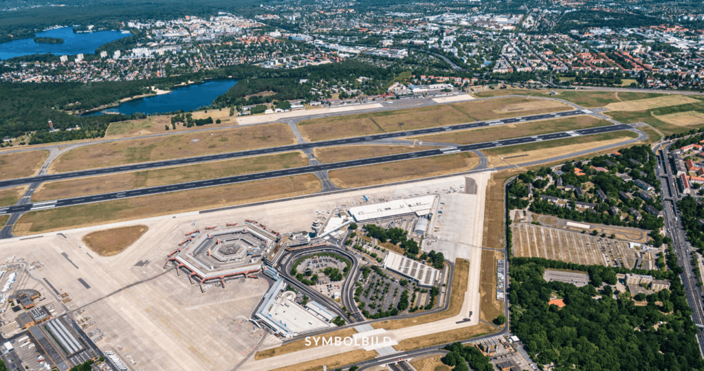 Das Bild zeigt eine Luftaufnahme des ehemaligen Flughafens Berlin Tegel. Zu den Hauptmerkmalen gehören eine lange Landebahn und ein Terminal mit mehreren Fluggastbrücken. Um den Flughafen herum befinden sich Grünflächen, Straßen und Gewässer. SYMBOLBILD Schumacher Quartier