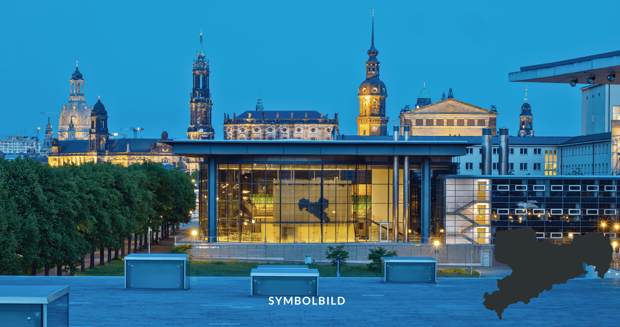 Im Vordergrund befindet sich ein modernes Glasgebäude mit eingeschaltetem Licht, das die Silhouette einer Reiterstatue zeigt. Dahinter sind historische Gebäude mit Türmen und aufwendiger Architektur zu sehen, die gegen den Abendhimmel beleuchtet sind. Außenansicht des Plenarsaals mit Blick auf die Dresdner Altstadt. SYMBOLBILD Sachsen Landtagswahl