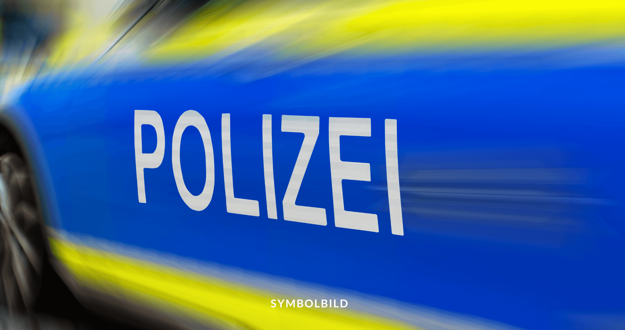 Das Bild zeigt die Seite eines Fahrzeugs mit dem Wort “POLIZEI” in großen, weißen Großbuchstaben auf einem blauen Hintergrund. Der Hintergrund ist verschwommen und zeigt gelbe und blaue Streifen, was auf Bewegung oder Geschwindigkeit hindeutet. SYMBOLBILD Rassistisch motivierte Tat in Brandenburg: Flüchtlingsunterkunft mit Schweineblut beschmiert