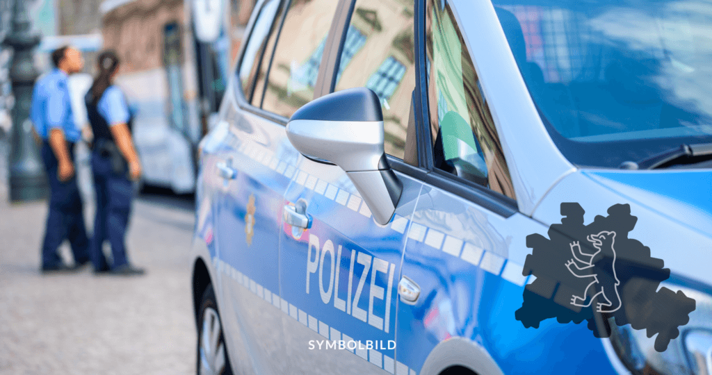 Das Bild zeigt einen Teil eines Polizeiautos mit dem Schriftzug “POLIZEI”. Der Fokus liegt auf dem Seitenspiegel und einem Teil der Tür des blau-silbernen Autos. Im Hintergrund sind verschwommene Figuren von zwei Polizisten. SYMBOLBILD Kundgebung "Stoppt die Kriegsverbrechen" in Berlin mit Festnahmen und Ermittlungen.