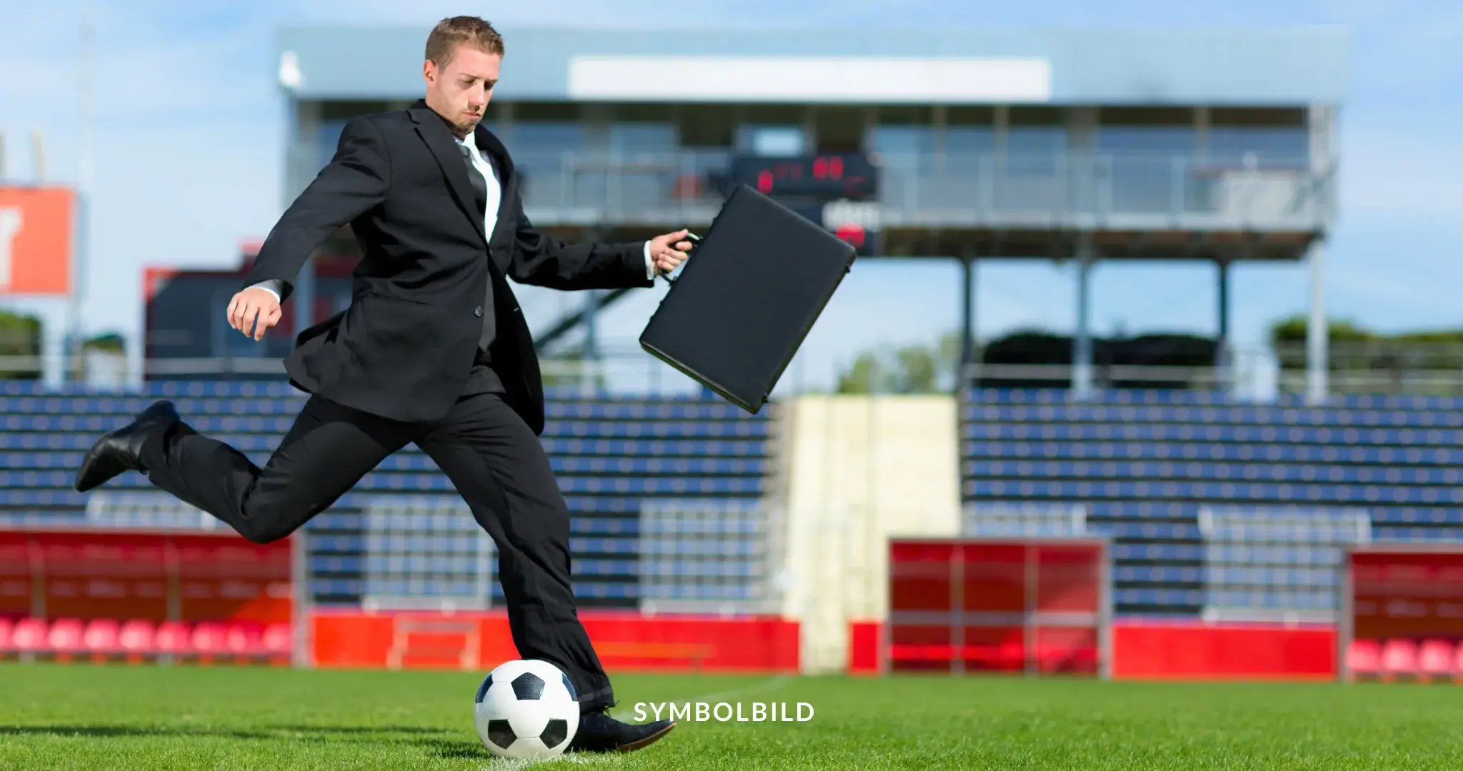 Das Bild zeigt eine Person in einem Business-Anzug, die auf einem Rasenfeld einen Fußball tritt. Im Hintergrund sind ein Tor und Tribünen zu sehen. SYMBOLBILD FIFA EuGH Urteil zu Transferbestimmungen im Fußball