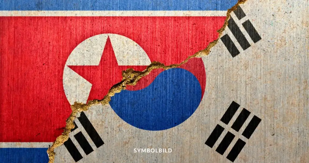 Das Bild zeigt eine symbolische Darstellung der Teilung zwischen Nordkorea und Südkorea. Im Hintergrund sieht man die Flaggen beider Länder, mit der nordkoreanischen Flagge links und der südkoreanischen rechts. Die Flaggen sind auf einer rauen, texturierten Oberfläche dargestellt, und ein prominenter Riss verläuft diagonal durch die Mitte, was die Trennung und Spannungen zwischen den beiden Nationen symbolisiert. SYMBOLBILD Nordkorea sprengt Grenzverbindungen – Spannungen eskalieren auf der koreanischen Halbinsel