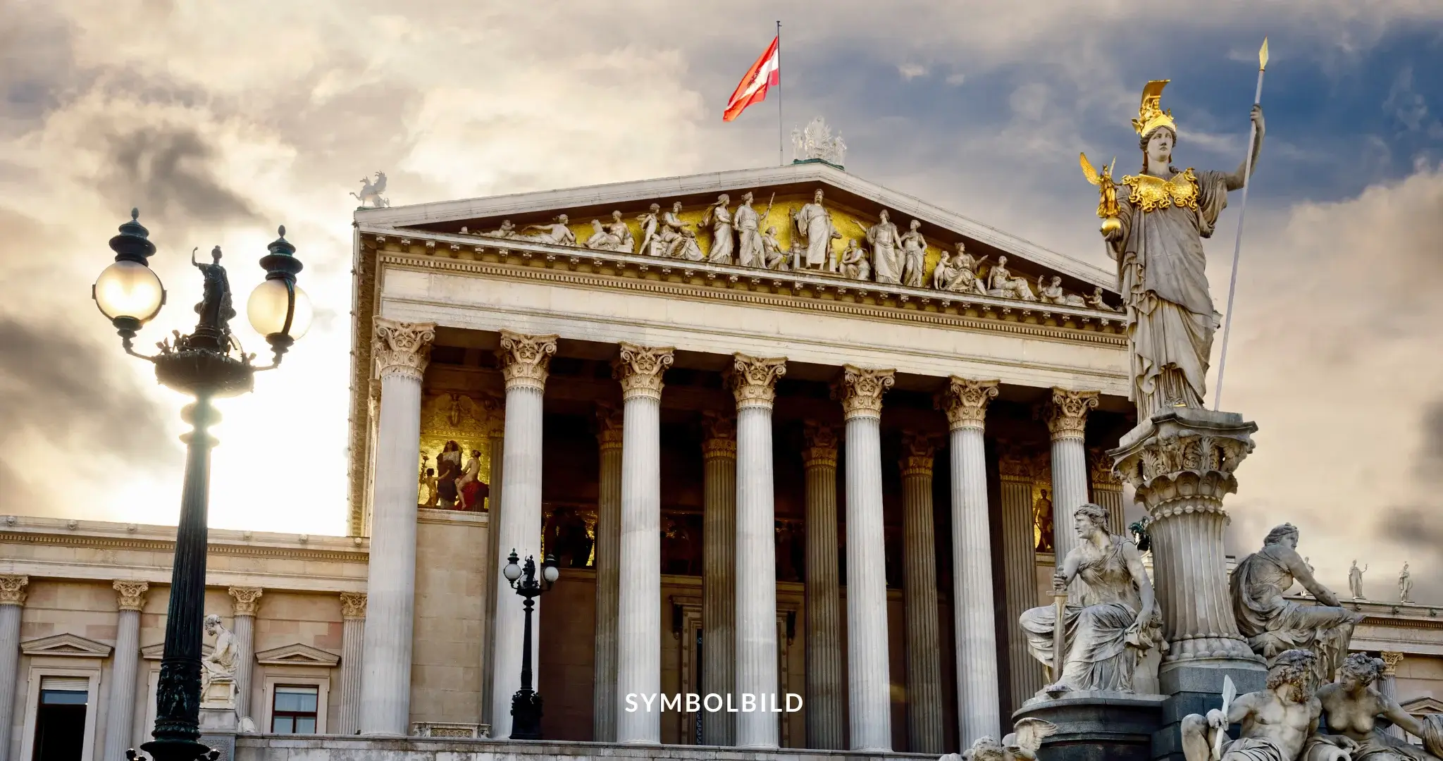 Das Bild zeigt das österreichische Parlament in Wien. Das Gebäude ist ein beeindruckendes Beispiel für neoklassizistische Architektur mit großen Säulen, die ein mit Skulpturen verziertes Giebeldreieck stützen. Über dem Giebel weht die österreichische Flagge vor einem teilweise bewölkten Himmel. Vor dem Gebäude steht der Pallas-Athene-Brunnen, mit einer markanten Statue der Göttin Athene, die mit Speer und Schild ausgestattet ist. Links im Bild sind Straßenlaternen zu sehen, die zur klassischen Atmosphäre beitragen. SYMBOLBILD FPÖ-Sieg in Österreich löst Proteste aus