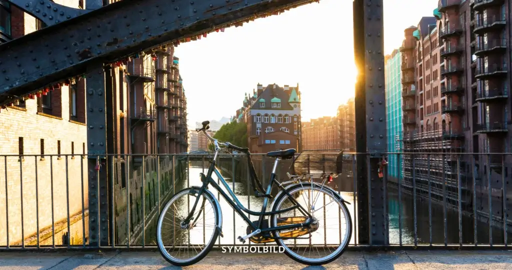 Ein Fahrrad steht auf einer Brücke, die mit Nieten geschmückt und mit kleinen Schlössern behangen ist. Dahinter erstreckt sich die Hamburger Speicherstadt entlang eines Kanals, erleuchtet von der zwischen den Gebäuden durchscheinenden Sonne. SYMBOLBILD Volksbegehren Schluss mit Gendersprache in Hamburg gescheitert