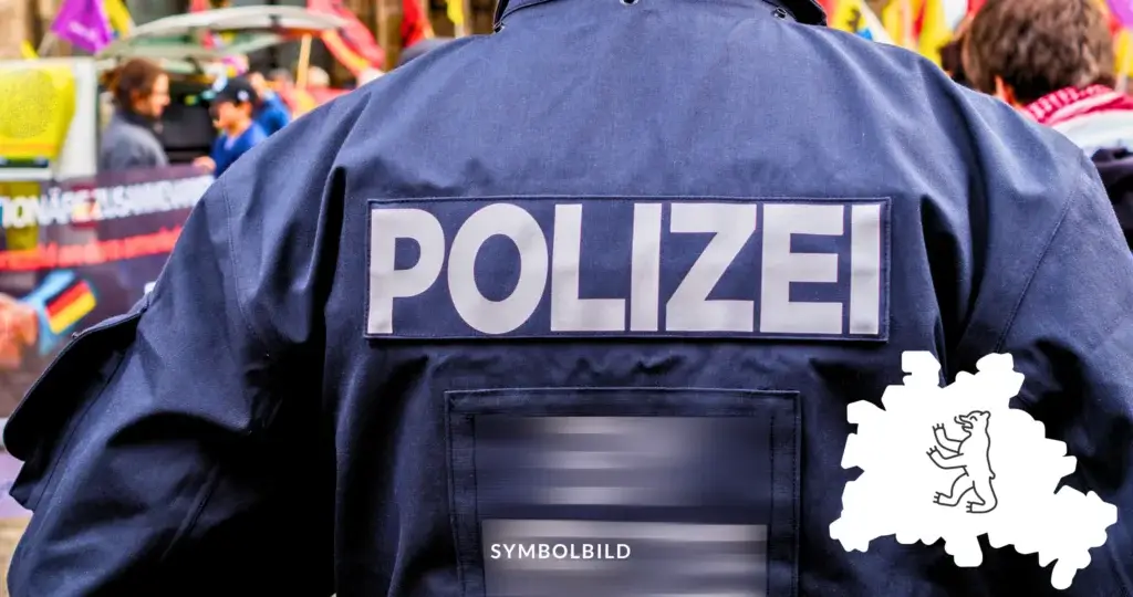 Das Bild zeigt den Rücken einer Person, die eine Jacke mit der Aufschrift „POLIZEI“ trägt. Im Hintergrund ist eine verschwommene Szene zu sehen, die auf eine Versammlung hindeutet. Symbolbild Ausschreitungen bei Protesten in Berlin zum Nahostkonflikt