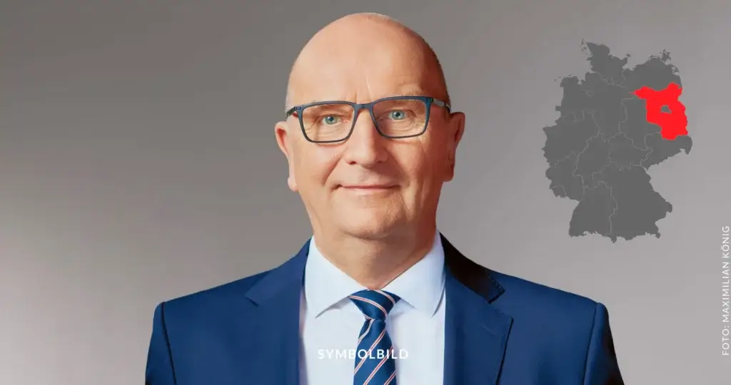 Das Bild zeigt Dietmar Woidke, den Ministerpräsidenten von Brandenburg. Er trägt einen blauen Anzug, ein weißes Hemd und eine blaue Krawatte mit roten und weißen Streifen. Rechts von ihm ist eine Karte von Deutschland zu sehen, auf der Brandenburg rot markiert ist. SYMBOLBILD Dietmar Woidke als Ministerpräsident von Brandenburg erneut gewählt