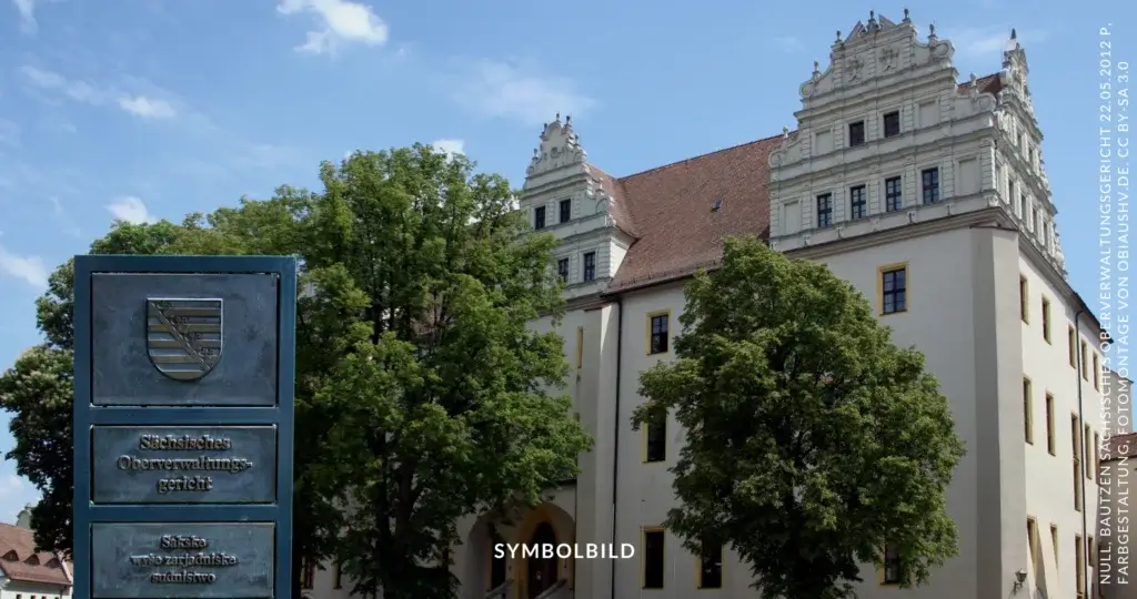 Das Bild zeigt das Sächsische Oberverwaltungsgericht. Im Vordergrund ist ein Schild mit dem Wappen und der Aufschrift "Sächsisches Oberverwaltungsgericht" sowie der sorbischen Übersetzung "Sakske wšo zarjadniske sudnistwo" zu sehen. Im Hintergrund befindet sich das Gebäude des Gerichts, das durch seine historische Architektur und die markanten Giebel auffällt. Symbolbild Urteil zur Mohrenstraße in Radebeul durch Oberverwaltungsgerichts