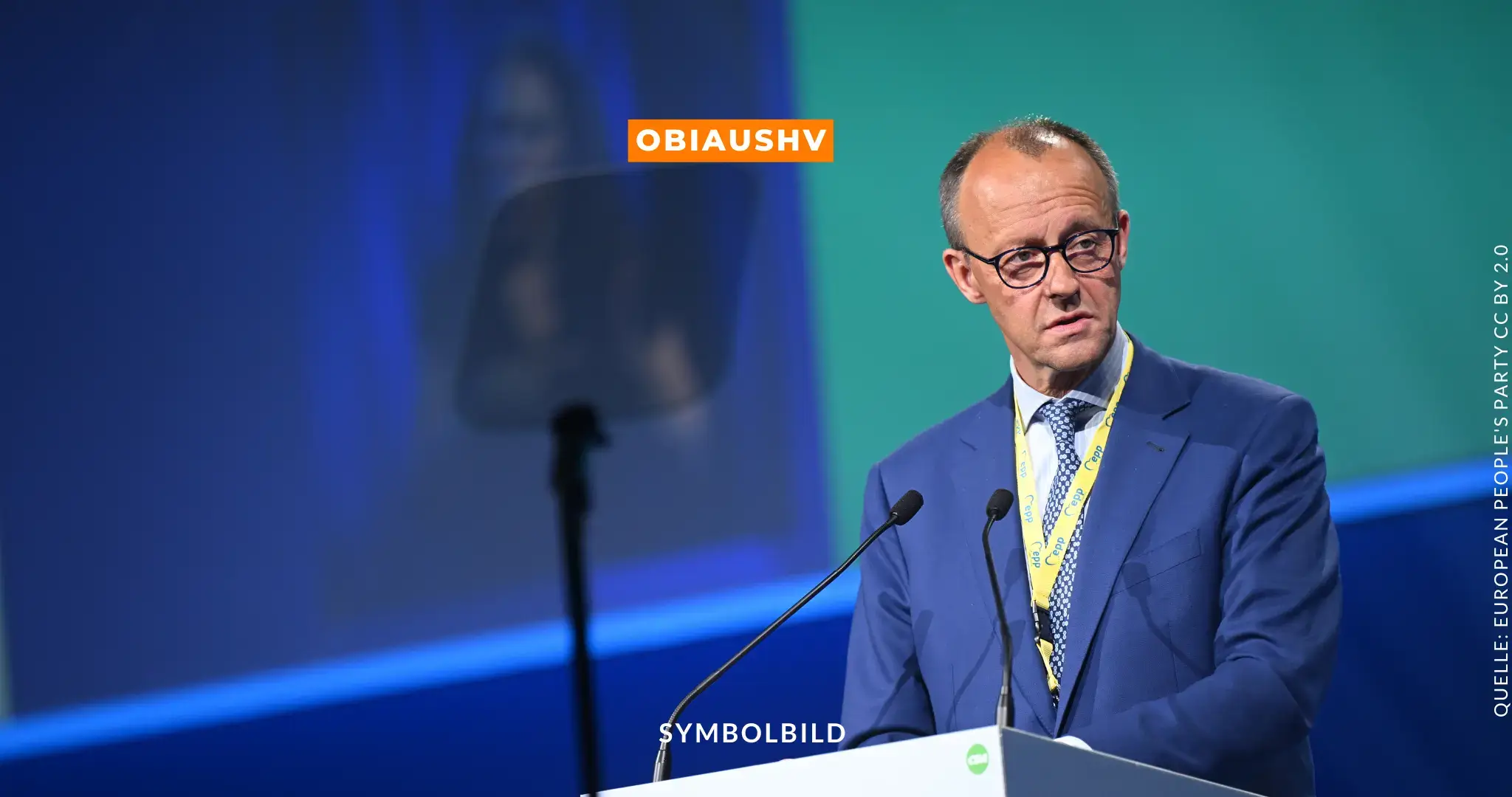 Das Bild zeigt Friedrich Merz, einen deutschen Politiker der CDU, während einer öffentlichen Rede. Er trägt einen blauen Anzug, ein weißes Hemd und eine gemusterte Krawatte. Ein gelbes Lanyard hängt um seinen Hals. Im Hintergrund ist ein bläulich-grüner Hintergrund zu sehen, und es gibt eine Leinwand mit einem Mikrofon vor ihm sowie einen Teleprompter auf der linken Seite. Oben in der Mitte des Bildes steht in einem orangefarbenen Kasten der Text „OBIAUSHV“, und unten in der Mitte steht in weißer Schrift „SYMBOLBILD“. Auf der rechten Seite des Bildes ist der Text „QUELLE: EUROPEAN PEOPLE'S PARTY CC BY 2.0“ zu sehen. Symbolbild CDU-Parteitag Berlin 2025 – Friedrich Merz und das Sofortprogramm zur Asylpolitik